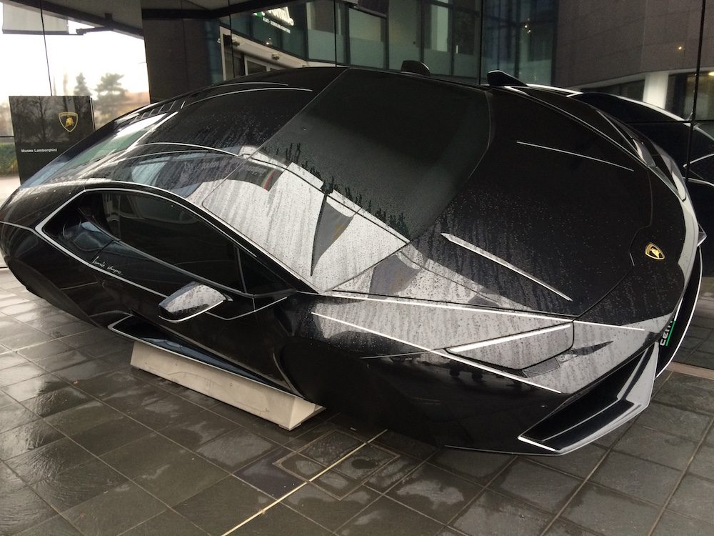 Outside the Lamborgini factory, there's an entire car leaning on its side at the front entrance